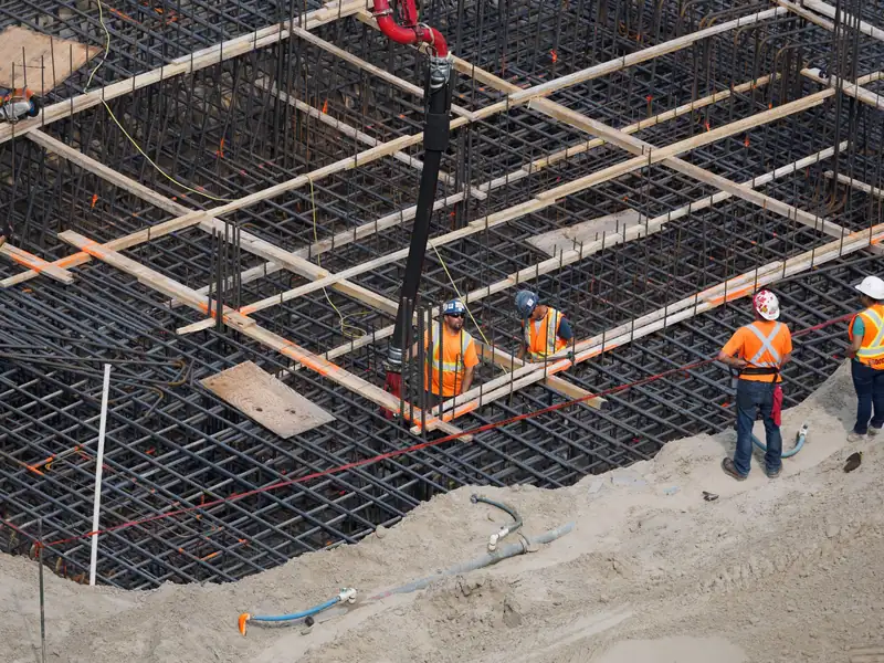 Crew in hard hats working inside a dense rebar mat with a concrete pump hose