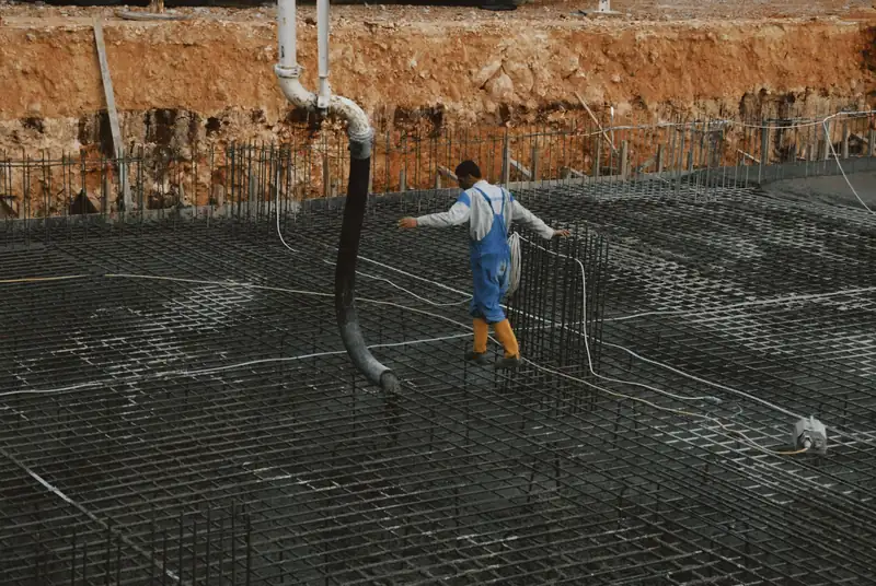 Worker on a rebar grid guiding a concrete pump hose during a large slab pour