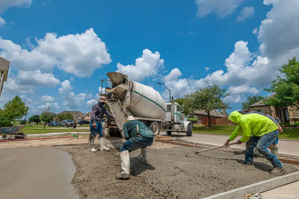 Concrete crew placing ready-mix from a truck chute into new driveway forms in a brick-home subdivision