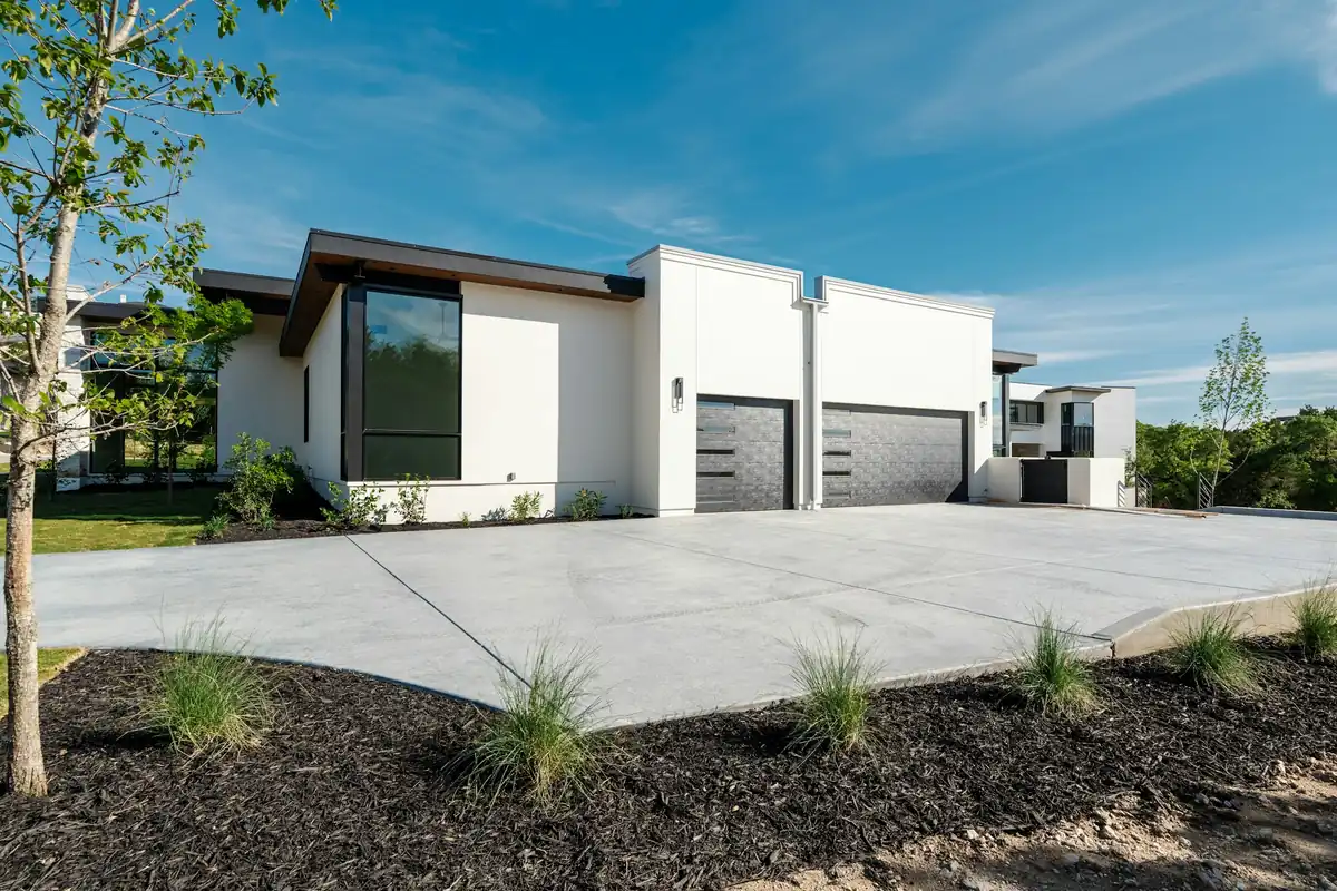 Very wide light-gray concrete driveway and apron in front of a modern white home