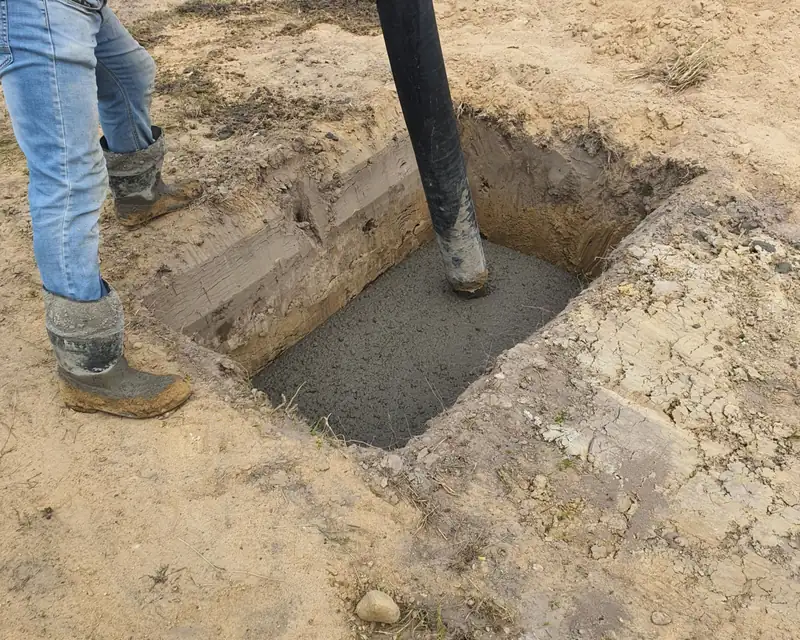Pump hose filling an excavated concrete footing while a worker guides the pour