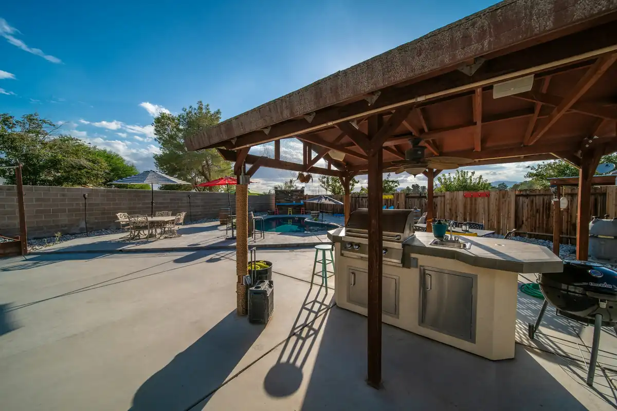 Large backyard concrete patio slab with a wood pavilion, outdoor kitchen and pool