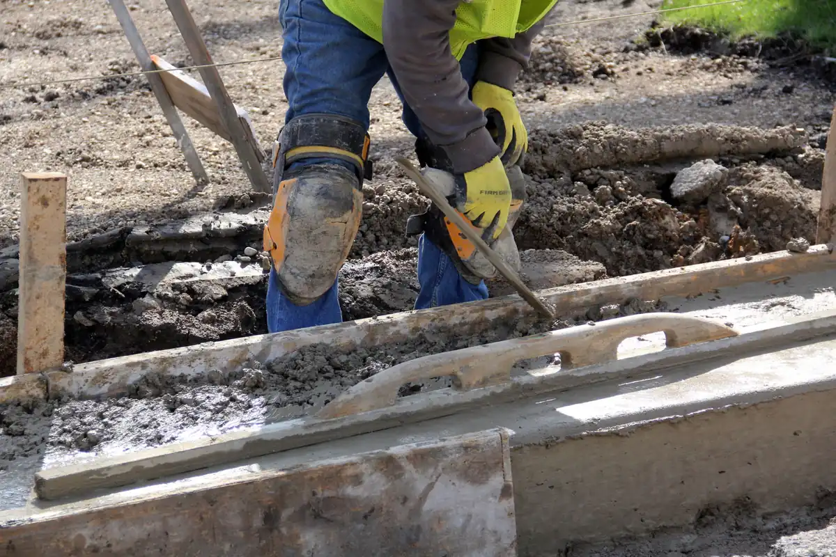 Finisher in knee pads working a fresh concrete surface along a form with a magnesium hand float