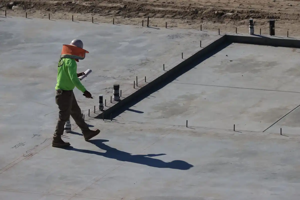 Fresh slab-on-grade concrete foundation with plumbing stub-outs and a worker crossing it