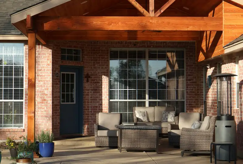 Cedar patio cover over a concrete slab behind a brick home, with a concrete pool deck
