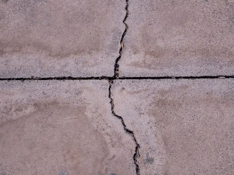Crack running across a control joint in a weathered concrete slab