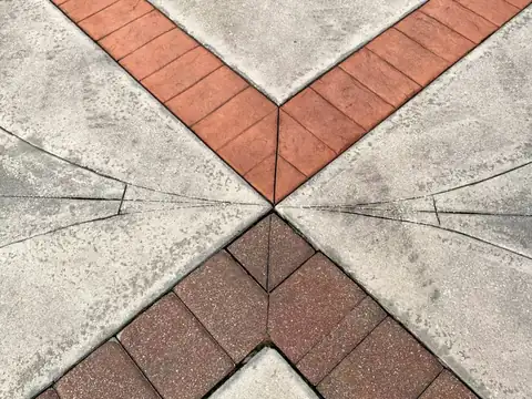 Decorative walk where red brick-pattern bands meet in a V between gray stone-textured fields