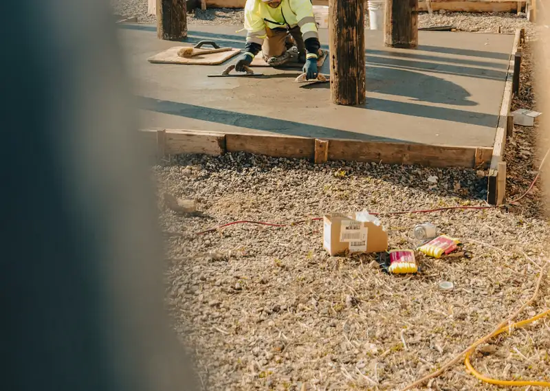 Finisher smoothing a freshly placed concrete slab with hand tools between timber posts