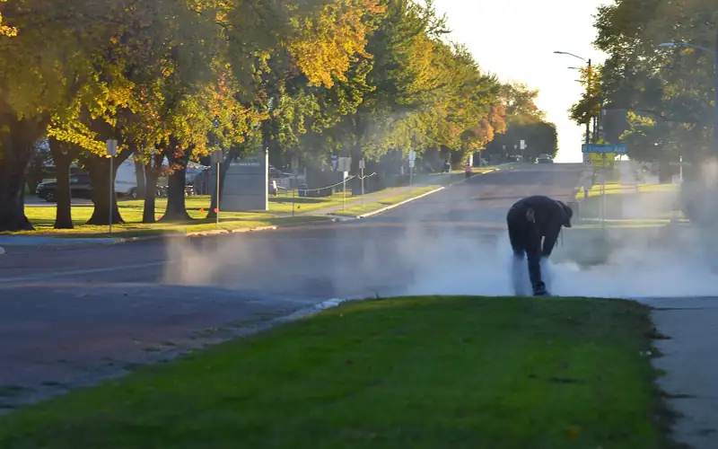 Worker saw-cutting concrete along a tree-lined residential street